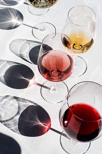 Creative photo of a simple clear wine glasses on a textured white background with sunlight and harsh shadows. red wine, white wine, rose wine, cognac, water and whiskey. Diverse alcohol drinks.