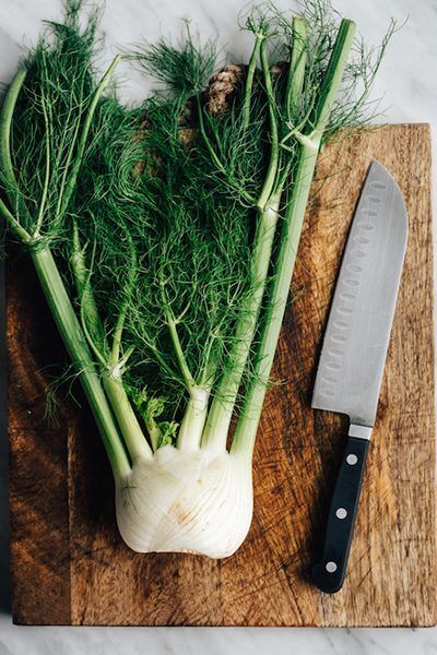 Whole fennel on a wooden cutting board with a chef's knife