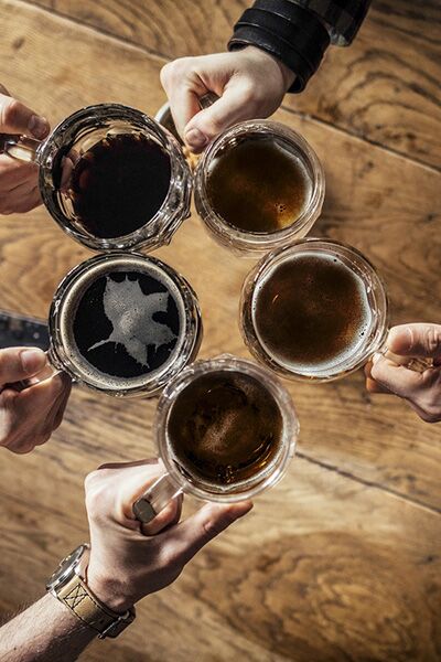 From above photo of hands of group of cropped unrecognisable men toasting with beer at bar.